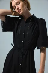 Vestido largo negro de popelina de algodón con alforzas, inserciones de encaje, manga corta abullonada, cuello camisero, botonadura frontal y cinturón fino para atar en la cintura.