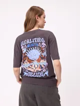 Remera de algodón con corte holgado, color crema, con estampado gráfico en la espalda que incluye un sol, montañas y mariposas con la frase Realities Rusty Collide.