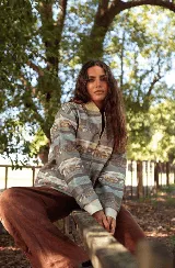 Campera de jean con cierre frontal y cuello tipo bomber, presenta un estampado horizontal con motivos paisajísticos y geométricos en tonos azules, marrones y beige. Posee puños de tela elástica en color blanco.