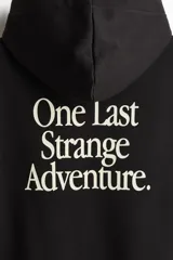 Canguro negro con capucha y bolsillo frontal tipo canguro. Presenta un estampado gráfico en el pecho con el logo de la serie Stranger Things y una silueta del Mind Flayer sobre un atardecer.