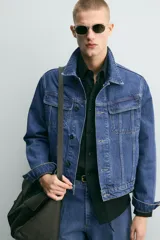 Cazadora de denim de algodón con corte relajado, cuello solapa, cierre frontal de botones y mangas largas con puños abotonados. Presenta bolsillos de solapa en el pecho y bolsillos laterales de vivo, con un acabado de efecto lavado.