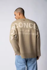 Sweater oversize de tejido de punto en color gris, con cuello redondo, puños y ruedo acanalados con detalles de desgaste. Presenta un diseño minimalista con logo tejido en la espalda.
