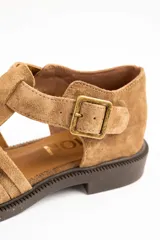 Sandalias cangrejeras de gamuza color visón, con diseño de tiras entrelazadas, tira ajustable con hebilla metálica en el tobillo y suela plana de goma marrón.
