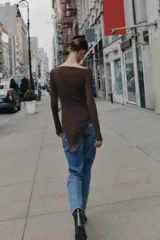 Camiseta de manga larga confeccionada en viscosa, con cuello barco y ajuste slim fit. Presenta un diseño con drapeado lateral y un bajo asimétrico decorado con una aplicación de encaje.
