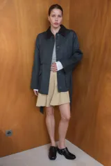 Chaqueta encerada de corte recto con cuello de solapa en pana marrón. Presenta manga larga, bolsillos delanteros de vivo y de plastrón con solapa, y un cinturón de lazada en el mismo tejido. Incluye cierre frontal con botones ocultos por tapeta y abertura en la espalda.