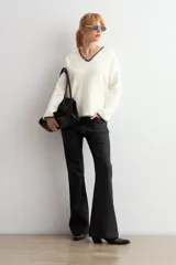 Sweater de punto color crudo con escote en V, manga larga y detalles de bordado en color negro en el escote y los puños.
