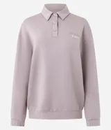 Buzo deportivo de corte oversized color lila, con cuello polo y cierre frontal con botones a presión. Presenta mangas largas con puños ajustados y una estampa bordada en el pecho. Confeccionado en una mezcla de poliéster, modal y elastano.