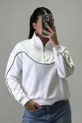 Buzo deportivo color beige con cuello alto y cierre frontal parcial. Presenta costuras decorativas con ribetes blancos en el pecho y a lo largo de las mangas. Posee puños y ruedo elásticos.