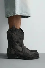 Bota estilo cowboy fabricada en tejido denim de algodón con efecto lavado, diseño de caña media con tiradores laterales, horma cuadrada y tacón ancho.