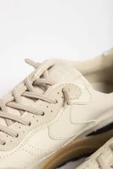 Zapatillas deportivas color crema con detalles en beige, negro y blanco.