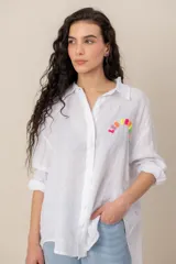 Camisa blanca de lino de corte oversize, con mangas largas y detalle de bordado colorido en el pecho.