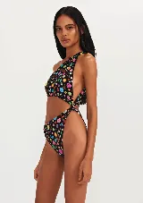 Traje de baño enterizo negro con estampado de símbolos y dibujos de colores. Diseño de un solo hombro con abertura en la cintura.