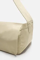 Bolso de hombro de diseño minimalista confeccionado en tejido de algodón. Cuenta con un compartimento principal con cierre de solapa con doble imán y botón a presión, además de bolsillos interiores. Incluye asa de hombro fija.