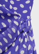Vestido corto de poliéster con estampado de lunares, cuello en pico cruzado y diseño evasé. Presenta tirantes anchos y cierre mediante lazo lateral.
