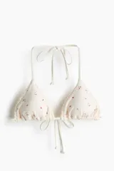 Top de bikini de triángulo de color crudo con pequeño estampado floreado y ribete fruncido en los bordes. Cuenta con tiras para anudar en la espalda y en el cuello.