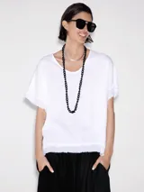 Blusa blanca de lino con cuello redondo y mangas cortas con terminación desflecada.