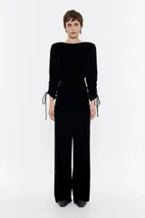 Mono largo de terciopelo negro, con corte ajustado en la cintura, escote barco con abertura en la espalda y mangas largas con volumen en los puños ajustables con cordones.