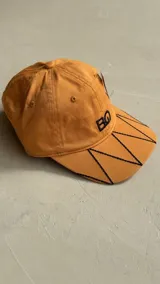 Gorra negra con bordado de las iniciales BG en el frente y diseño de costuras geométricas en la visera.