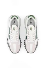 Championes New Balance de estilo casual, con capellada en gamuza color gris claro, logo "N" en verde oscuro y suela de goma con diseño texturizado en gris oscuro.