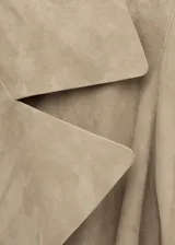 Gabardina larga de piel caprina en color beige, con solapas amplias, cierre cruzado con botones y cinturón ajustable del mismo material.