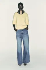 Jersey de punto color amarillo pálido, con cuello redondo y mangas cortas. Presenta un calce oversize y aberturas caladas en los laterales inferiores.