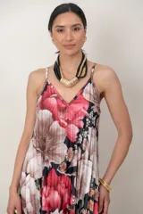 Vestido largo de seda plisada con estampado floral en tonos rojos, rosados y blancos sobre base oscura, con tirantes finos y escote en V.