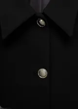 Chaqueta corta de corte recto y diseño crop, con cuello camisero y cierre frontal de botones metálicos. Presenta manga larga y forro interior.