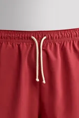Short de baño rojo de tejido técnico ligero y elástico, con cintura elástica ajustable mediante cordón blanco y aberturas laterales en las perneras.