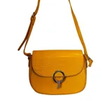 Cartera tipo bandolera color amarillo, con solapa frontal de textura efecto cocodrilo y cuerpo liso. Presenta un cierre metálico circular con detalle colgante plateado y correa larga ajustable.