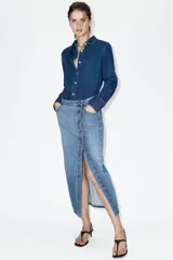 Falda midi de denim azul con diseño cruzado, cierre frontal con botones metálicos y bolsillos delanteros.