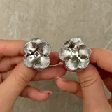 Par de aros tipo caravanas con diseño de flor de cuatro pétalos con textura estriada en acabado plateado.