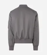 Campera tipo bomber de color verde militar, con cierre frontal, cuello, puños y cintura en tejido rib. Presenta bolsillos frontales con solapa y botón a presión, además de un bolsillo utilitario en la manga.