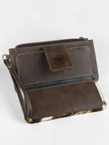 Billetera porta celular confeccionada en cuero marrón con detalle de pelo vacuno con estampado animal print tipo vaca en tonos blancos, marrones y negros. Cuenta con correa de muñeca y cierre superior.