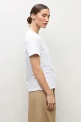 Remera blanca de manga corta con detalle de botones metálicos en el hombro, cuello redondo y corte clásico.