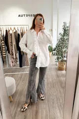 Camisa blanca de algodón con cuello clásico, cierre frontal con botones, mangas largas con puños abotonados y volados en el frente y los puños.