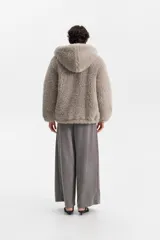 Campera de abrigo con textura peluda (tipo borrego o teddy), color gris topo, de calce amplio y con capucha. Posee cierre frontal.