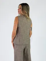 Chaleco sastrero sin mangas, de color beige con diseño de rayas verticales, cuello en V y cierre frontal con botones.