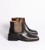 Bota corta de cuero vacuno en tono negro con efecto desgastado, de horma cuadrada y taco bajo de madera. Presenta un panel elástico lateral en color marrón y cierre interno para facilitar el calce.