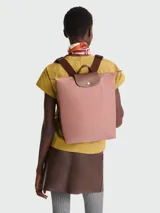 Mochila de diseño minimalista en color beige, con solapa y asa superior en cuero marrón texturizado. Cuenta con correas ajustables en color marrón y cierre principal.