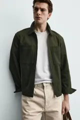 Sobrecamisa negra de corte relajado, confeccionada en tejido con mezcla de algodón elástico. Presenta cuello solapa, cierre frontal de cremallera, bolsillos de plastrón en el pecho y bolsillos de vivo en la cadera.