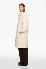 Abrigo midi de estructura envolvente confeccionado en mezcla de lana doble faz. Presenta cuello subido, cierre frontal con botones, mangas largas amplias con ajuste de botón en el puño y bolsillos laterales de vivo.