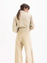 Pantalón wide leg de gabardina color beige, de tiro medio, con recortes diagonales y pespuntes a la vista que aportan volumen, bolsillos delanteros y pasadores en la cintura.