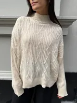 Sweater color crema con cuello alto y diseño de trenzas.
