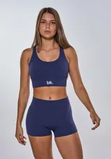 Conjunto deportivo compuesto por un top de escote redondo con banda elástica inferior y logo estampado, y un short de tiro alto ajustado. Ambas piezas son de color azul marino.