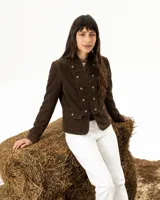 Chaqueta de gamuza color chocolate con diseño de estilo militar, cuello mao, cierre frontal y doble fila de botones metálicos vintage. Cuenta con dos bolsillos frontales con solapa y botones a juego.