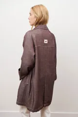 Spolverino largo de jean color azul, con cuello camisero, botones frontales y costuras decorativas en blanco.