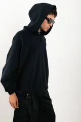 Buzo negro de corte amplio con capucha y detalle de parche circular en el pecho.
