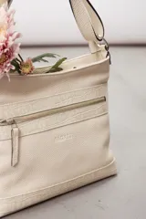 Cartera de cuero color beige, de diseño estructurado, con bolsillo frontal con cierre y detalles en cuero grabado con efecto reptil. Cuenta con correa ajustable para llevar al hombro o cruzada.