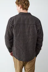 Camisa de manga larga confeccionada en franela con estampado a cuadros en tonos oscuros. Presenta cuello clásico, cierre frontal con botones, puños abotonados y un bolsillo aplicado en el pecho.