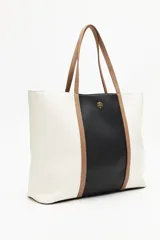 Cartera tipo tote bag en símil cuero, con diseño en bloques de color negro y blanco, y detalles en marrón. Tiene asas largas para llevar al hombro y un cierre magnético.